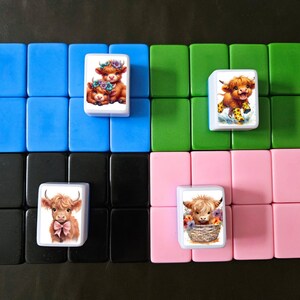 May include: Four white tiles with colorful images of Highland cows. The tiles are arranged in a 2x2 grid on a black, blue, green, and pink background.