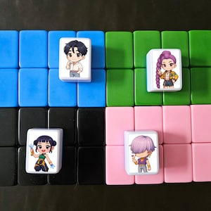 May include: A collection of colorful Mahjong tiles arranged in a grid. Four tiles feature anime-style character illustrations. The tiles are set against a background of blue, green, pink, and black tiles, creating a visually appealing pattern.