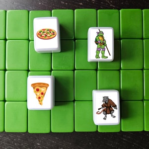 May include: A set of four white tiles with images of pizza and cartoon characters. The tiles are on a green surface.