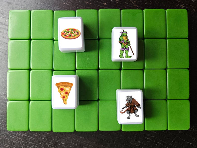 May include: A set of four white tiles with images of pizza and cartoon characters. The tiles are on a green surface.