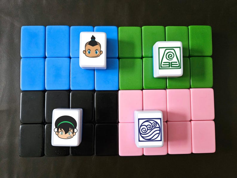 May include: A set of colorful tiles arranged in a grid, with four tiles featuring cartoon character illustrations. The tiles are blue, green, pink, and black, with white tiles displaying character art. The background is a dark surface.