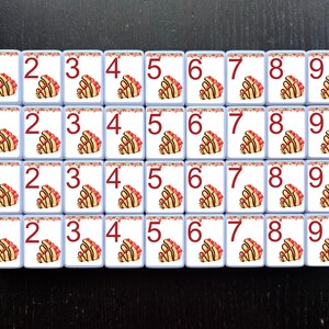 May include: A set of 36 white tiles with red numbers 1 through 9. Each tile has a decorative design of a pastry with red and white frosting.