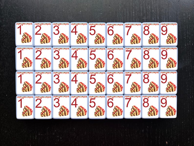 May include: A set of 36 white tiles with red numbers 1 through 9. Each tile has a decorative design of a pastry with red and white frosting.