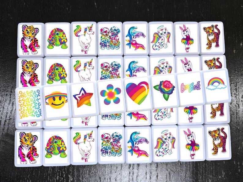 Op de afbeelding: Een set van 25 kleurrijke tegels met verschillende afbeeldingen, waaronder een regenboog hart, een eenhoorn, een bloem, een smiley, een ster, een dolfijn, een kat, een konijn, een tijger, een schildpad en een luipaard. De tegels zijn wit met een zwarte rand.