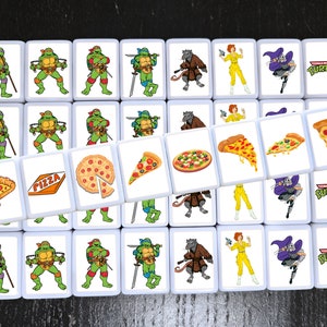 May include: A set of 25 white square tiles with images of Teenage Mutant Ninja Turtles characters, pizza slices, and pizza boxes. The tiles are arranged in a grid pattern. The tiles feature the words "Teenage Mutant Ninja Turtles" and "Pizza".