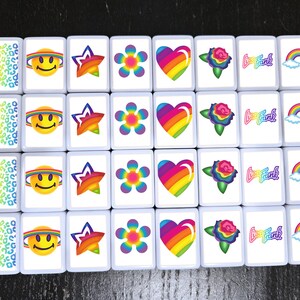 Op de afbeelding: Een set van 20 witte vierkante tegels met kleurrijke ontwerpen. De ontwerpen omvatten een regenboog hart, een regenboog bloem, een regenboog ster, een regenboog smiley, een regenboog roos, een regenboog met wolken en de tekst "Love Frank".