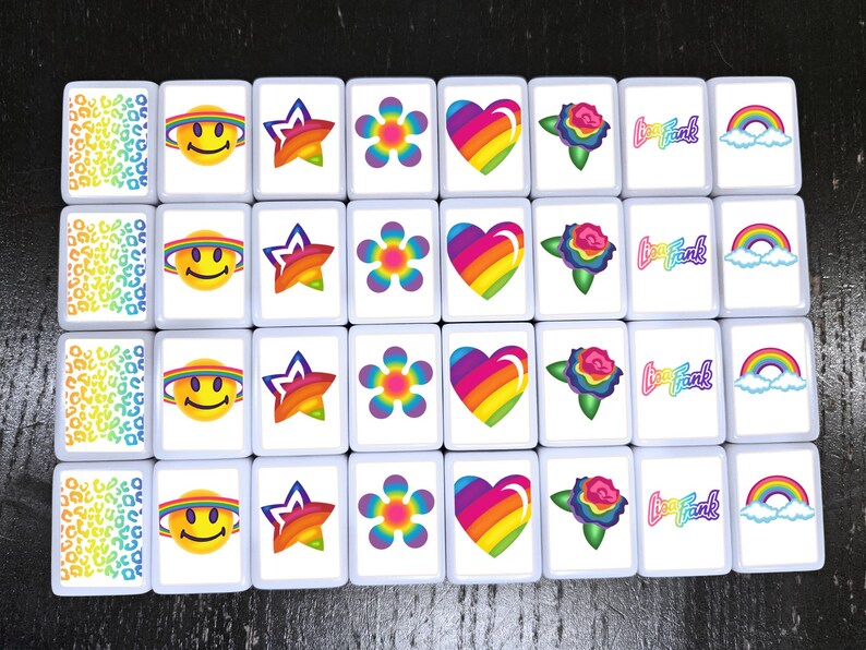 Op de afbeelding: Een set van 20 witte vierkante tegels met kleurrijke ontwerpen. De ontwerpen omvatten een regenboog hart, een regenboog bloem, een regenboog ster, een regenboog smiley, een regenboog roos, een regenboog met wolken en de tekst "Love Frank".