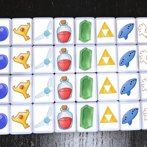 May include: A set of 16 white square tiles with different images on each. The images include a blue bomb, a gold key, a blue fairy, a red potion bottle, a green emerald, a yellow triangle, a blue ocarina, and a white chicken.