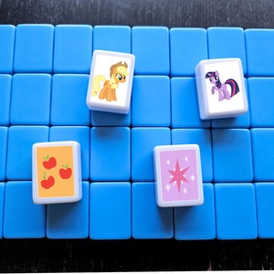 May include: A blue game board with four white tiles. Each tile features a different My Little Pony character. The characters are Applejack, Twilight Sparkle, Pinkie Pie, and Rainbow Dash.