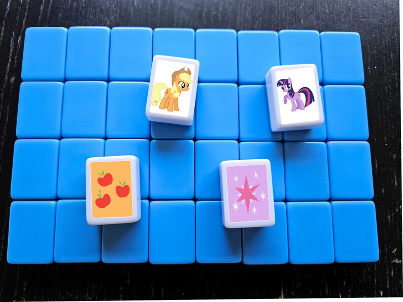 May include: A blue game board with four white tiles. Each tile features a different My Little Pony character. The characters are Applejack, Twilight Sparkle, Pinkie Pie, and Rainbow Dash.