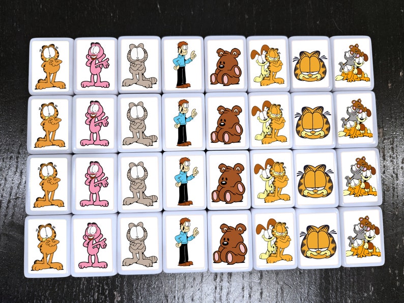 May include: A set of 24 white square tiles with colorful cartoon images of Garfield the cat. The tiles feature Garfield in various poses, including sitting, standing, and holding a plate of lasagna. There are also tiles with Garfield's friends, Odie the dog and Nermal the cat.