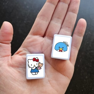 May include: Two white square tiles with cartoon characters. The first tile features Hello Kitty holding a small brown bear. The second tile features a blue penguin wearing a sailor hat and a red bow tie.