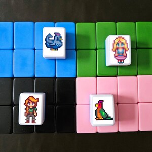 May include: A set of colorful tiles arranged in rows, featuring pixelated images of a chicken, a woman, a girl, and a parrot. The tiles are set against a black background, with blue, green, black, and pink tiles.