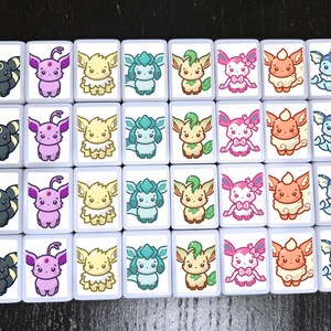 Puede incluir: Un conjunto de 24 azulejos de cer&aacute;mica blanca con im&aacute;genes de dibujos animados coloridos de varios personajes de Pok&eacute;mon. Cada azulejo presenta un Pok&eacute;mon diferente, incluyendo Eevee, Vaporeon, Jolteon, Flareon, Espeon, Umbreon, Leafeon, Glaceon, Sylveon, y otros.
