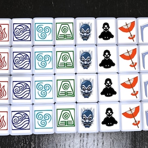 May include: A set of white tiles featuring various symbols and characters from a popular animated series. The tiles display images of fire, water, air, earth, and characters in red, blue, green, and black. The tiles are arranged in rows and columns.
