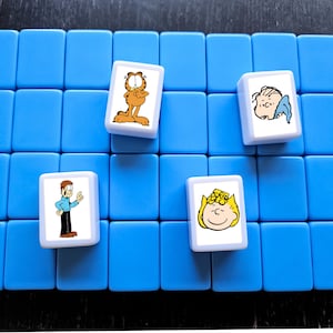 May include: Four cartoon character tiles on a blue background. The tiles are white with a cartoon character on each. The characters are Garfield, Snoopy, Lucy, and Linus.