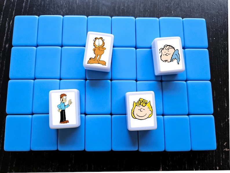 May include: Four cartoon character tiles on a blue background. The tiles are white with a cartoon character on each. The characters are Garfield, Snoopy, Lucy, and Linus.