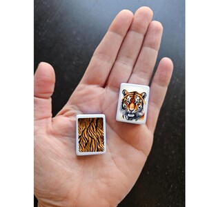 May include: Two small white square tiles with images of a tiger. One tile shows a tiger's face, and the other tile shows a tiger's stripes.