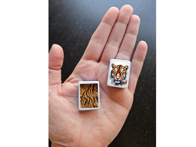 May include: Two small white square tiles with images of a tiger. One tile shows a tiger's face, and the other tile shows a tiger's stripes.