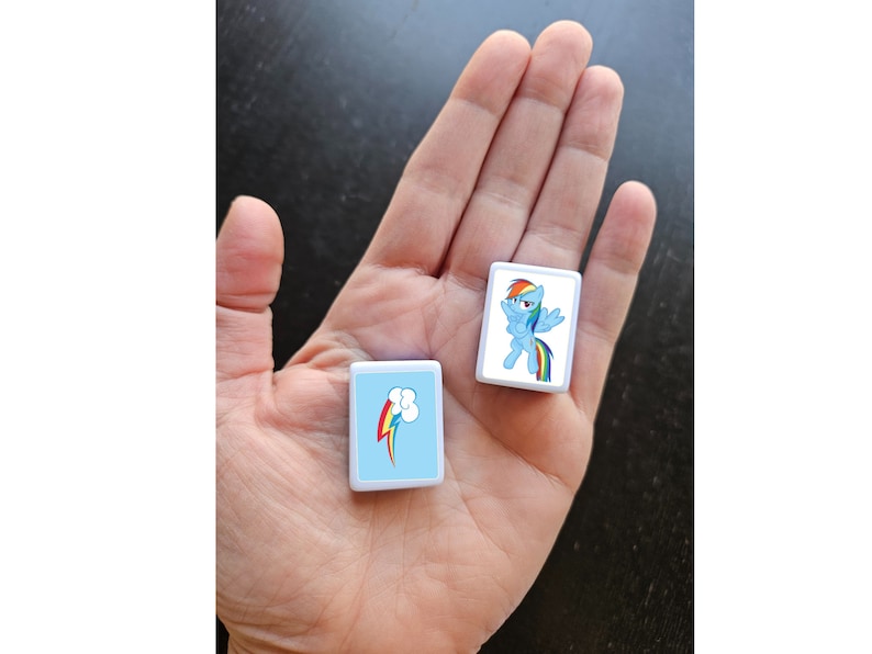 May include: Two white square tiles with blue backgrounds and images of a cartoon pony with a rainbow tail and mane. One tile shows the pony with wings spread, the other tile shows a rainbow with a cloud.