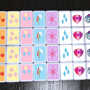 May include: A set of 16 colourful square tiles with various images, including apples, butterflies, balloons, a rainbow, a star, diamonds, a heart with a shield, and the words "My Little Pony".