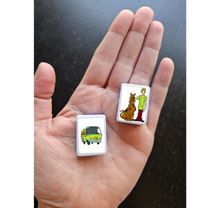 May include: Two white square tiles with images of characters from the Scooby Doo cartoon. One tile shows Scooby Doo and Shaggy, the other tile shows the Mystery Machine van.