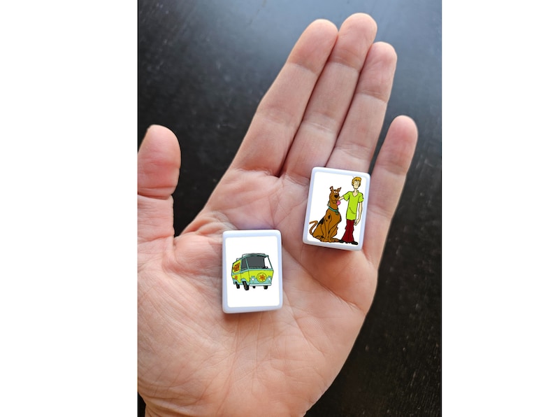 May include: Two white square tiles with images of characters from the Scooby Doo cartoon. One tile shows Scooby Doo and Shaggy, the other tile shows the Mystery Machine van.