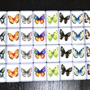 May include: A collection of 30 square tiles, each featuring a watercolor butterfly design. The butterflies vary in color, including blue, orange, green, black, and multi-colored wings. The tiles are arranged on a dark surface.