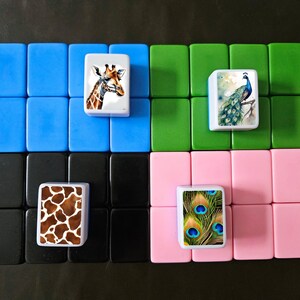 May include: Four sets of blue, green, black, and pink tiles with images of a giraffe, a peacock, a giraffe print, and a peacock feather print.