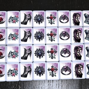 May include: A set of 20 white square tiles with various gothic-themed images. The images include a crescent moon, a skull, a high-heeled shoe, a jeweled cross, a ring, a woman with long dark hair, and a corset.