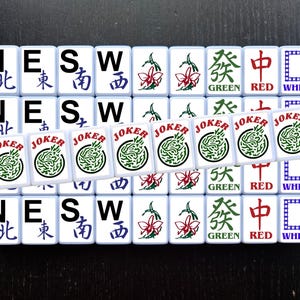 May include: A set of 16 white tiles with black lettering and colorful symbols. The tiles are arranged in a 4x4 grid. The tiles spell out "NESW" and have the words "North", "East", "South", "West", "Green", "Red", "White", and "Joker".