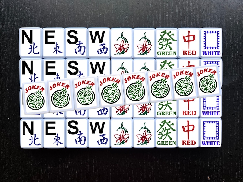 May include: A set of 16 white tiles with black lettering and colorful symbols. The tiles are arranged in a 4x4 grid. The tiles spell out "NESW" and have the words "North", "East", "South", "West", "Green", "Red", "White", and "Joker".