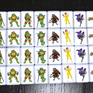 May include: A set of 16 white square tiles with images of Teenage Mutant Ninja Turtles characters. Each tile features a different character, including Leonardo, Donatello, Raphael, Michelangelo, Splinter, April O'Neil, and Shredder. The tiles also feature the Teenage Mutant Ninja Turtles logo.