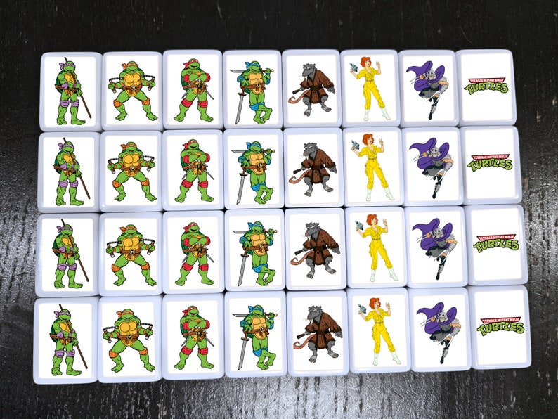 May include: A set of 16 white square tiles with images of Teenage Mutant Ninja Turtles characters. Each tile features a different character, including Leonardo, Donatello, Raphael, Michelangelo, Splinter, April O'Neil, and Shredder. The tiles also feature the Teenage Mutant Ninja Turtles logo.