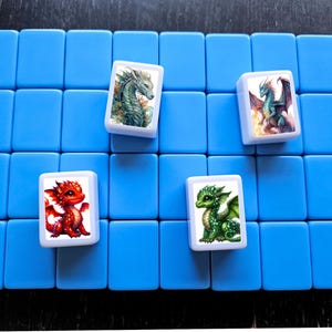 May include: Four white tiles with colorful dragon illustrations. The tiles are arranged on a blue background. The dragons are green, red, and blue.