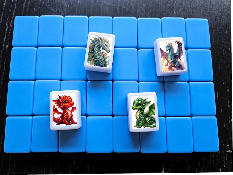 May include: Four white tiles with colorful dragon illustrations. The tiles are arranged on a blue background. The dragons are green, red, and blue.