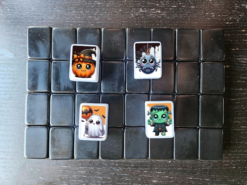 May include: A set of four square tiles with Halloween-themed illustrations. The tiles feature a pumpkin wearing a witch's hat, a spider, a ghost holding a balloon, and a green monster.