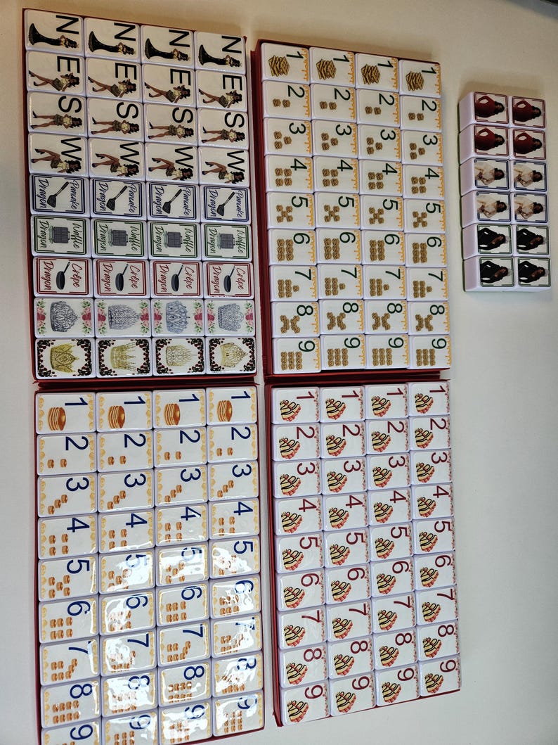 May include: A complete Mahjong set with white tiles featuring various symbols, numbers, and characters. The set includes tiles with the directions North, East, South, and West, along with dragon and flower tiles. The tiles are arranged in red boxes.