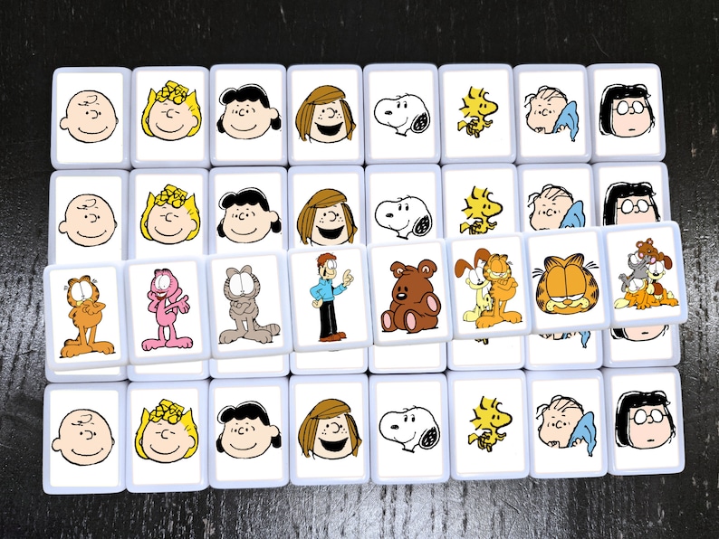 May include: A set of 36 white square tiles with cartoon images of characters from Peanuts, Garfield, and Snoopy. Each tile features a different character, including Charlie Brown, Lucy, Linus, Snoopy, Garfield, Odie, and Nermal.