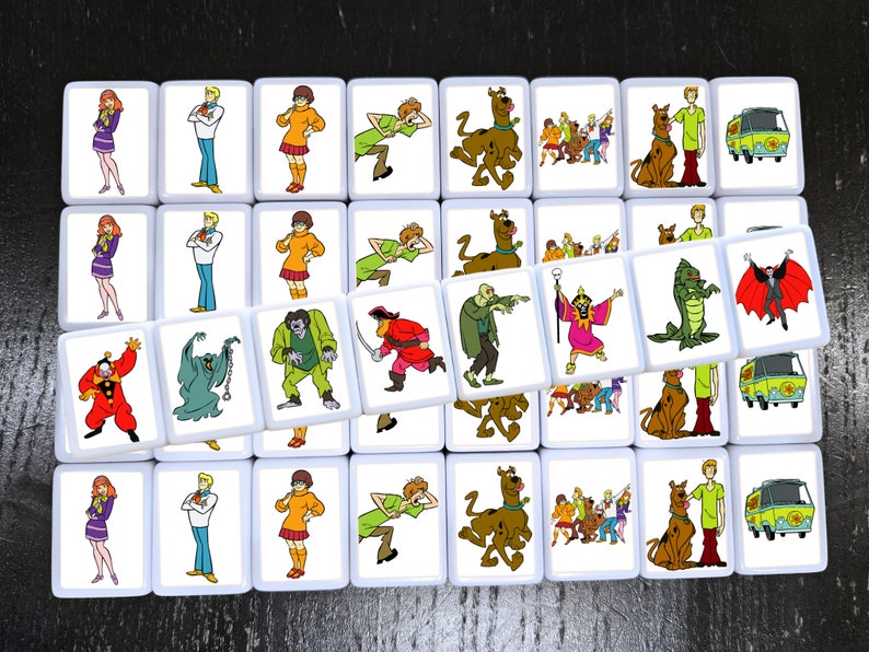 May include: A set of 24 square tiles featuring characters from the cartoon Scooby-Doo. Each tile has a different image, including Scooby-Doo, Shaggy, Velma, Daphne, Fred, and various monsters and villains. The tiles are white with a black border.