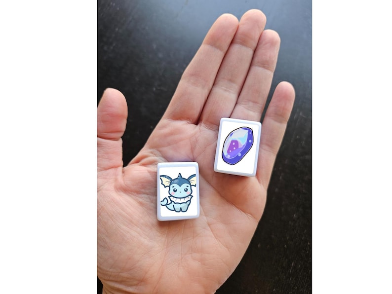 Puede incluir: Dos azulejos cuadrados blancos con im&aacute;genes de dibujos animados. Un azulejo presenta un Pok&eacute;mon de tipo agua azul y blanco de dibujos animados. El otro azulejo presenta una gema p&uacute;rpura y blanca de dibujos animados.