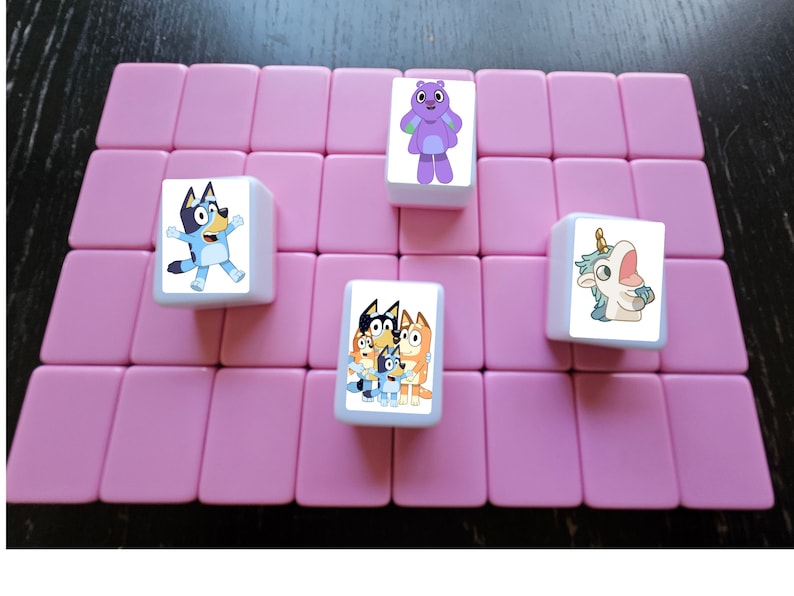 K&ouml;nnte beinhalten: Vier quadratische Fliesen mit Comicfiguren darauf. Die Fliesen sind wei&szlig; mit rosa R&auml;ndern und auf einer rosa Oberfl&auml;che angeordnet. Die Figuren sind ein blauer Hund, ein lila Monster, ein blaues Einhorn und eine Gruppe von drei blauen Hunden.