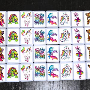 Op de afbeelding: Een set van 20 kleurrijke, vierkante tegels met verschillende afbeeldingen van dieren, waaronder een tijger, een schildpad, een eenhoorn, een paar dolfijnen, een kat met een halo en een konijn in een tutu. De tegels zijn wit met een zwarte omtrek.