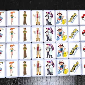 May include: A set of 16 white square tiles with images of Pokemon characters. Each tile features a different character, including Ash, Misty, Brock, and Team Rocket. The tiles also feature the Pokemon logo and the text "Gotta Catch 'Em All!"