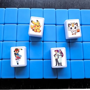 May include: A blue tile game board with four tiles featuring cartoon characters. The tiles have images of Pikachu, Meowth, Ash Ketchum, and Team Rocket. The game board is made of blue tiles.