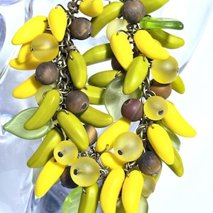 May include: A yellow and green beaded bracelet with a metal chain and wooden beads. The bracelet is made of small, banana-shaped beads.