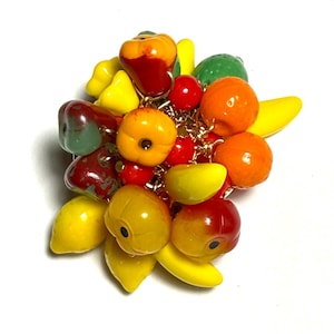 May include: A vintage fruit brooch with a collection of glossy fruit charms in various colours. The brooch includes red, orange, yellow, and green fruits, such as apples, oranges, lemons, and bananas, all linked by a gold-tone chain.