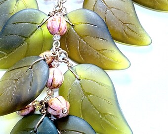 May include: A green leaf necklace with pink and gold beads. The leaves are made of glass and have a textured surface.