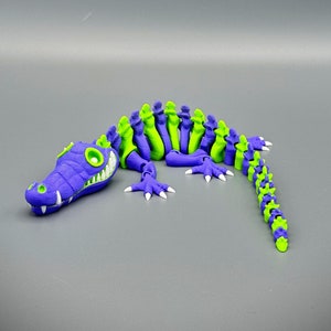Multi Colored 3D printed crocodile or alligator Skeleton. Purple head with white teeth, rest of skeleton alternator colors for the length of model. White eyes and claws.