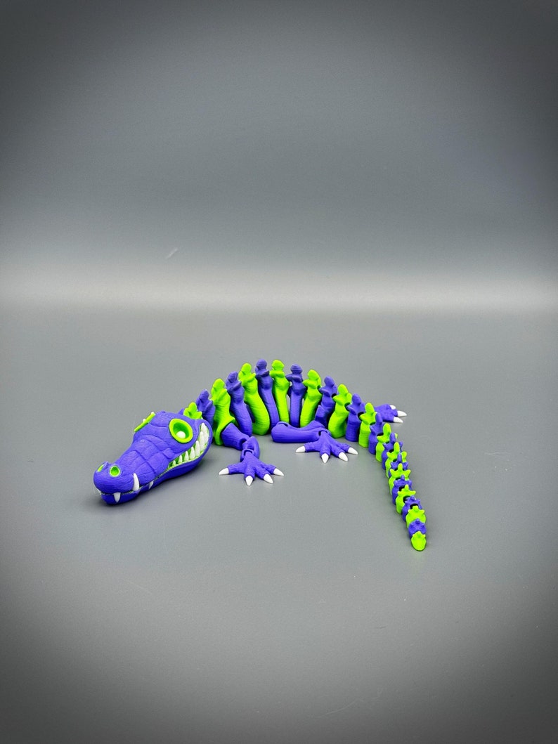 Multi Colored 3D printed crocodile or alligator Skeleton. Purple head with white teeth, rest of skeleton alternator colors for the length of model. White eyes and claws.
